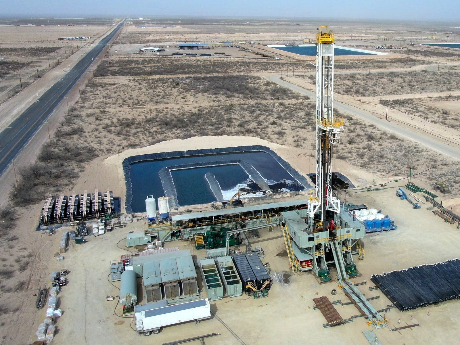 Aerial view of a drilling rig beside a lined produced water pit in an arid oilfield